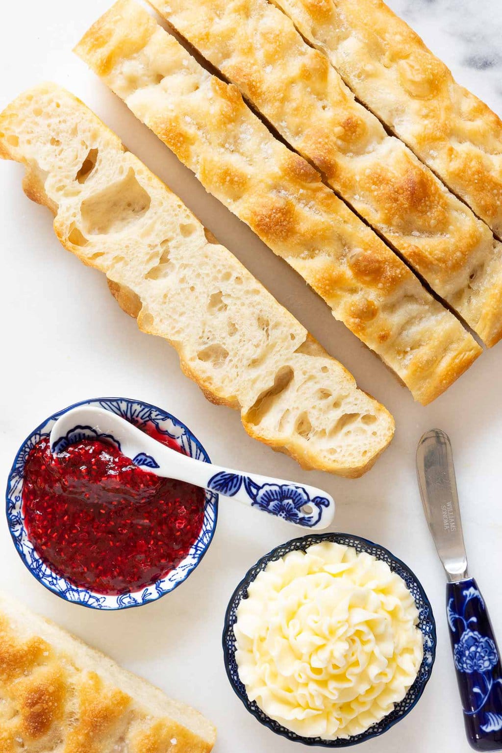 Vertical overhead photo of slices of Ridiculously Easy Same Day Focaccia bread and bowls of Raspberry jam and piped butter.