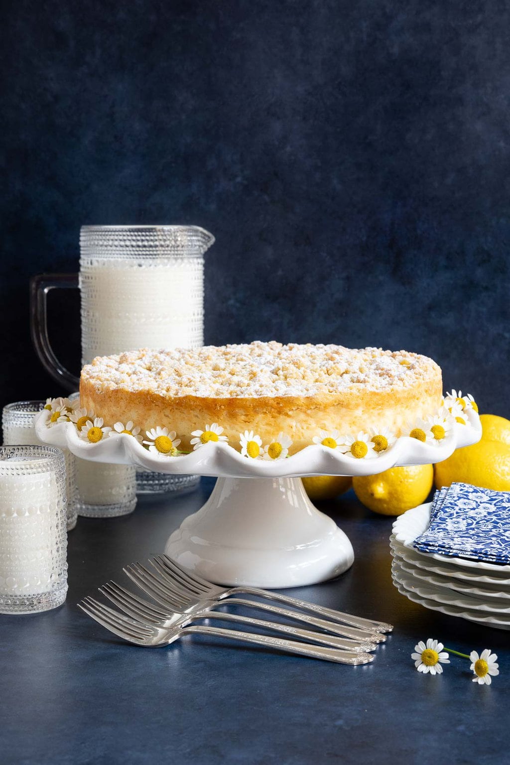 Italian Lemon Curd Ricotta Tart - thecafesucrefarine.com Vertical photo of a Italian Lemon Curd Ricotta Tart on a white scalloped pedestal serving plate.