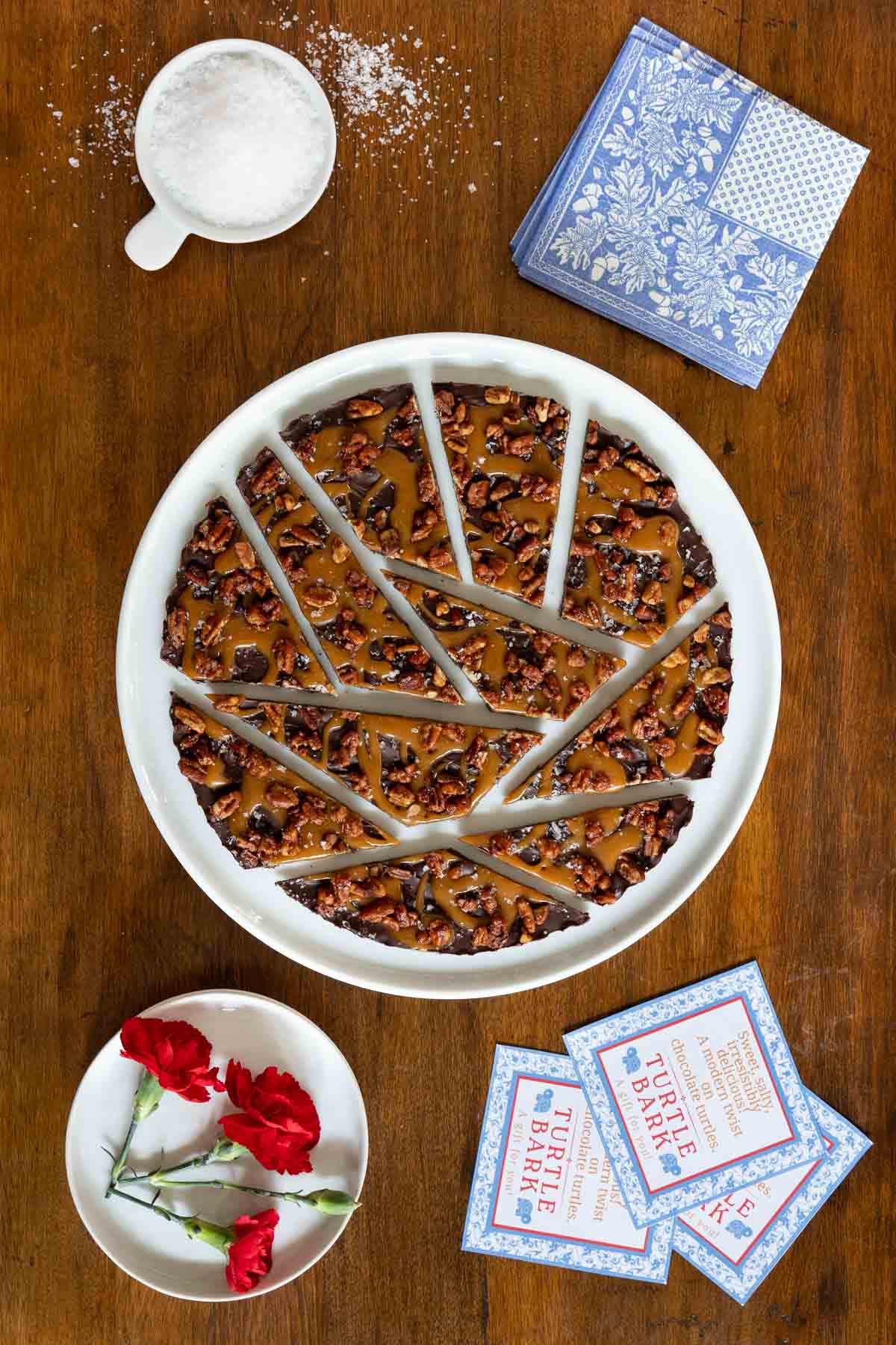 Vertical overhead photo of a batch of Ridiculously Easy Chocolate Caramel Turtle Bark on a white serving plate with custom Turtle Bark labels for gift giving.