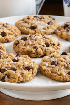 Horizontal closeup photo of a batch of Grandma's Chocolate Chip Oatmeal Cookies on a white pedestal serving plate.