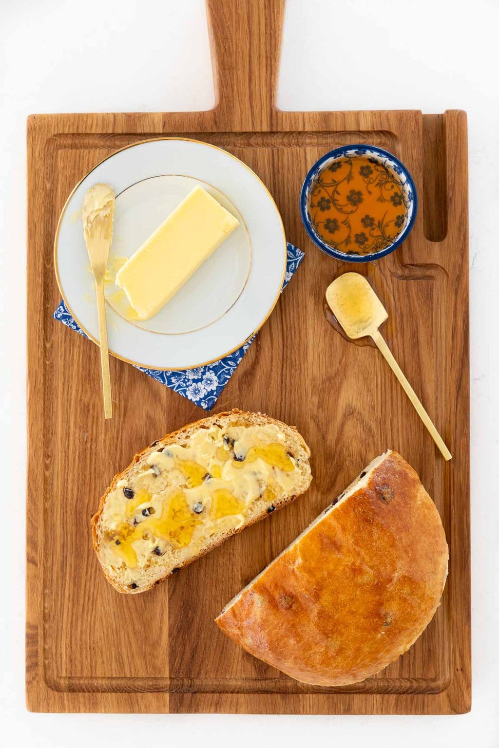 Overhead vertical photo of a sliced loaf of Irish Freckle Bread on a wood cutting board with Irish butter and honey on the slice.