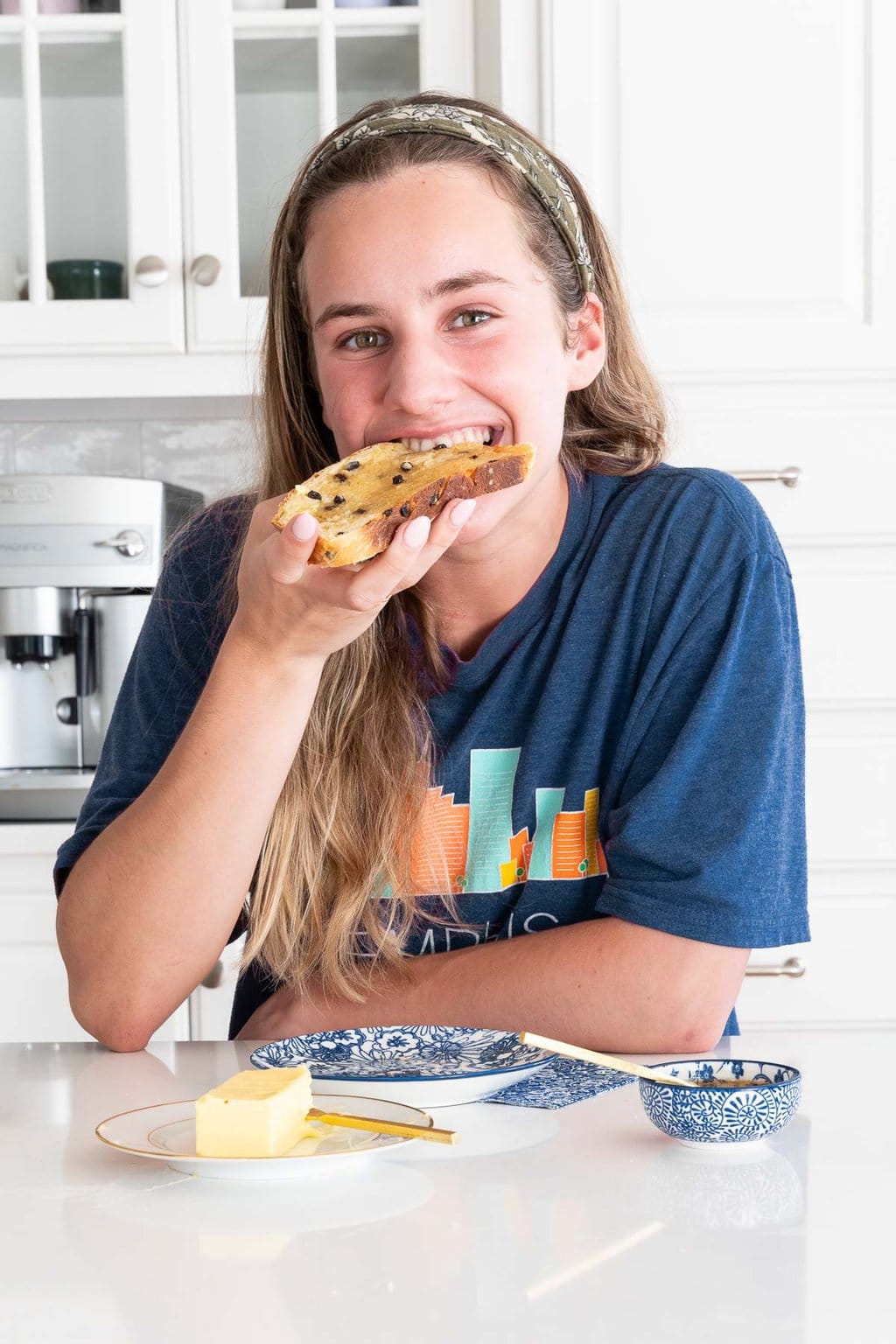 Vertical photo of Annie eating a slice of Irish Freckle Bread with honey and Irish butter.