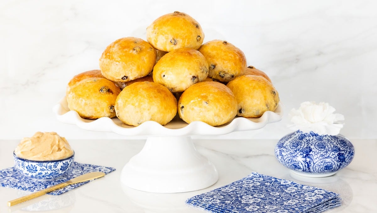 Horizontal photo of a batch of Irish Freckle Bread Rolls on a white scalloped serving plate with a dish of cinnamon honey butter on the left side.