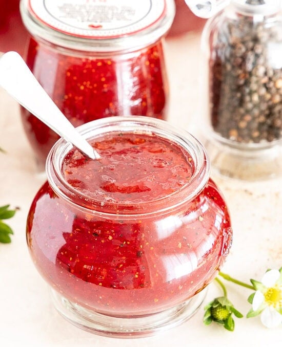 Horizontal photo of jars of Red, White and Black Strawberry Jam surrounded by fresh strawberries.