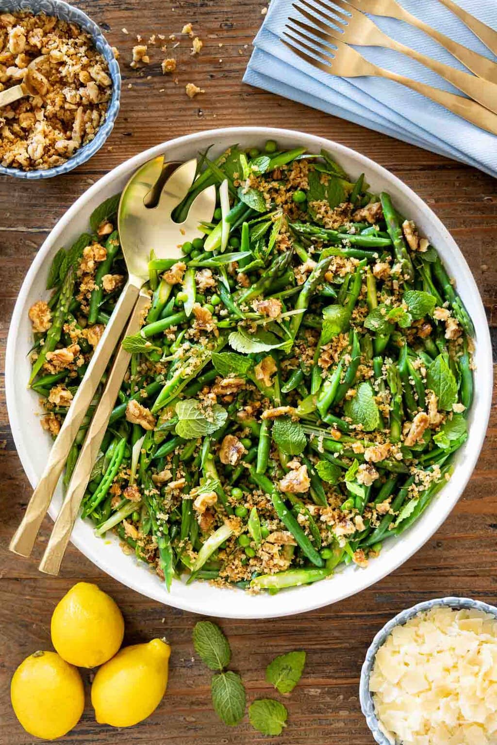 Vertical overhead photo of a Lemony French Green Bean Asparagus Salad on a wood table garnished with panko walnut topping and shaved Parmesan cheese.