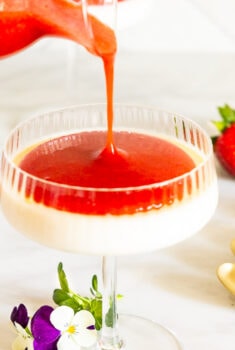 Horizontal photo of Ridiculously Easy Strawberry Coulis being poured over a dessert dish of Lemon Rosemary Panna Cotta.