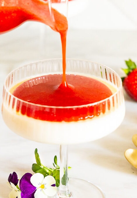 Horizontal photo of Ridiculously Easy Strawberry Coulis being poured over a dessert dish of Lemon Rosemary Panna Cotta.