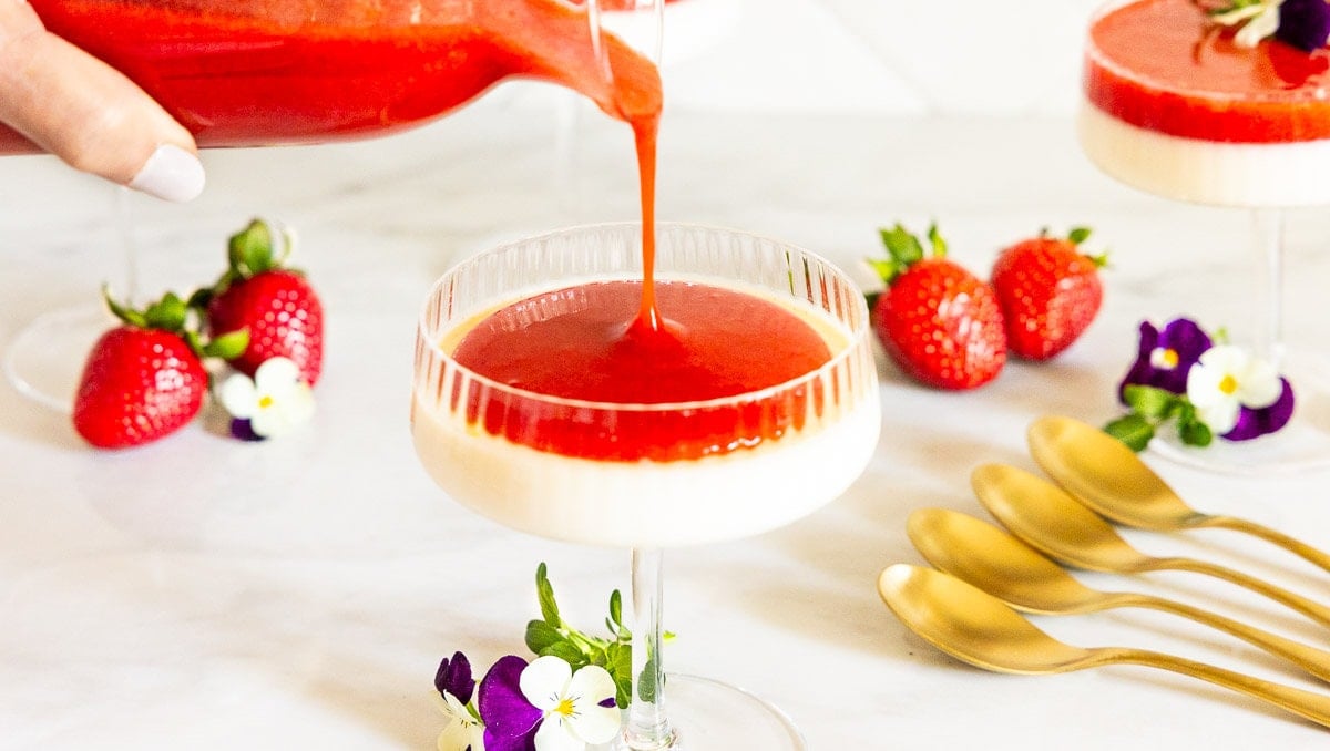 Horizontal photo of a person pouring Ridiculously Easy Strawberry Coulis over a dessert base of Lemon Rosemary Panna Cotta.