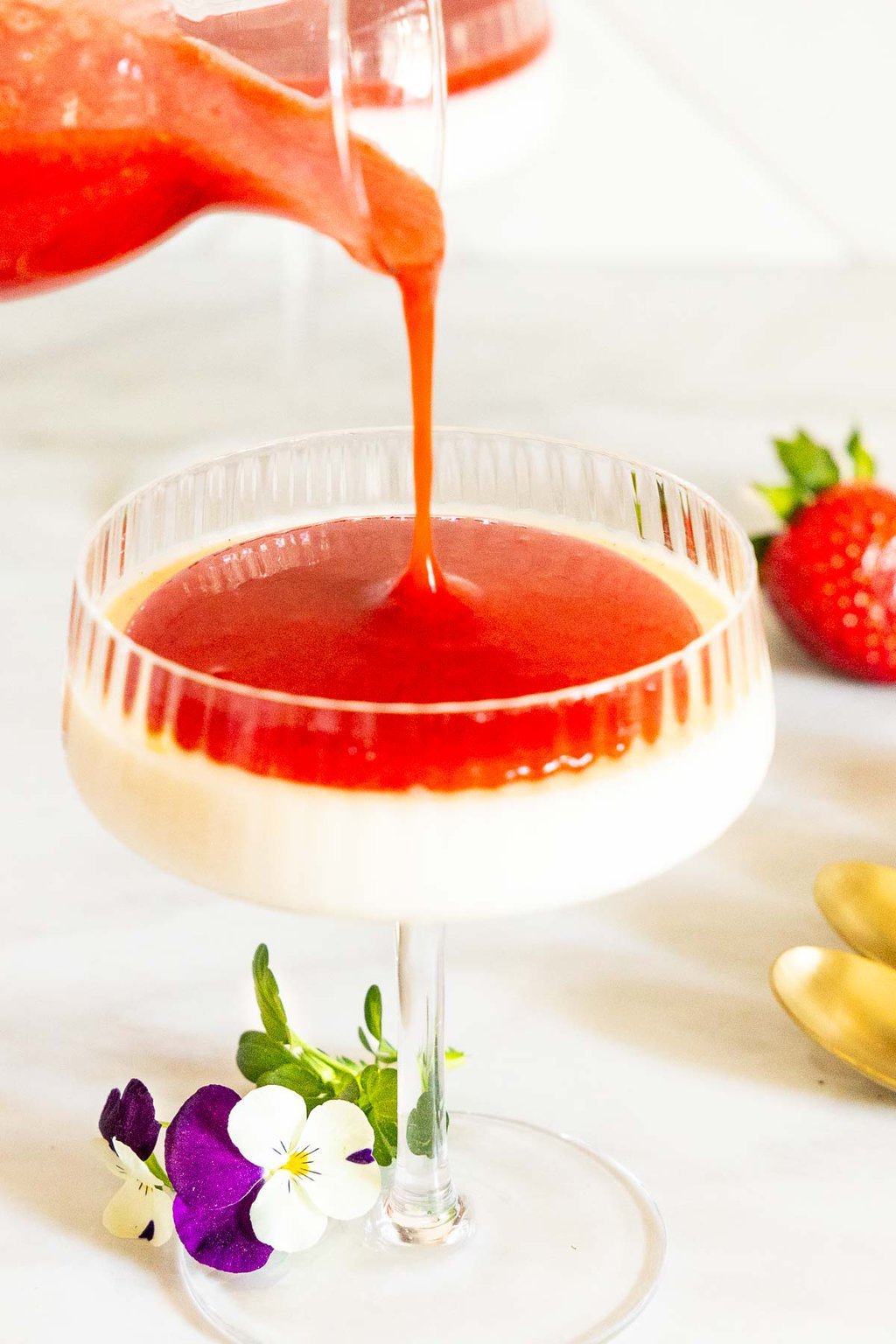 Vertical photo of Ridiculously Easy Strawberry Coulis being poured on top of a glass dessert dish of Lemon Rosemary Panna Cotta.