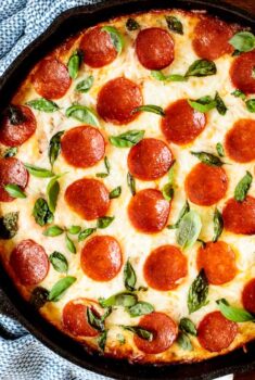 Horizontal overhead photo of a Deep Dish Pepperoni Pizza garnished with basil leaves on a wood table.