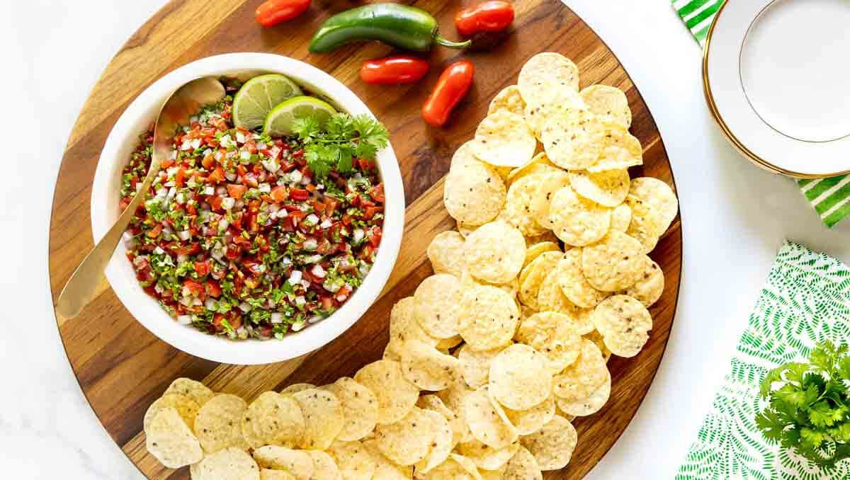 Horizontal overhead photo of a bowl of Best Ever Pico de Gallo (Salsa Mexicana) on a round wood appetizer board.