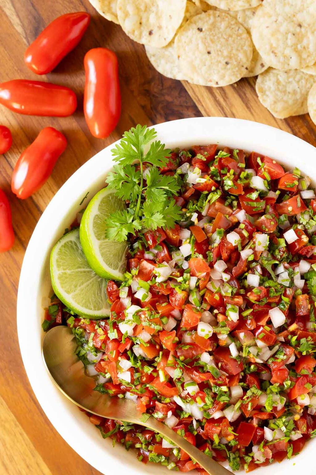 Best Ever Pico de Gallo (Salsa Mexicana) - thecafesucrefarine.com Vertical overhead closeup photo of a bowl of Best Ever Pico de Gallo (Salsa Mexicana) surrounded by red peppers and tortilla chips.