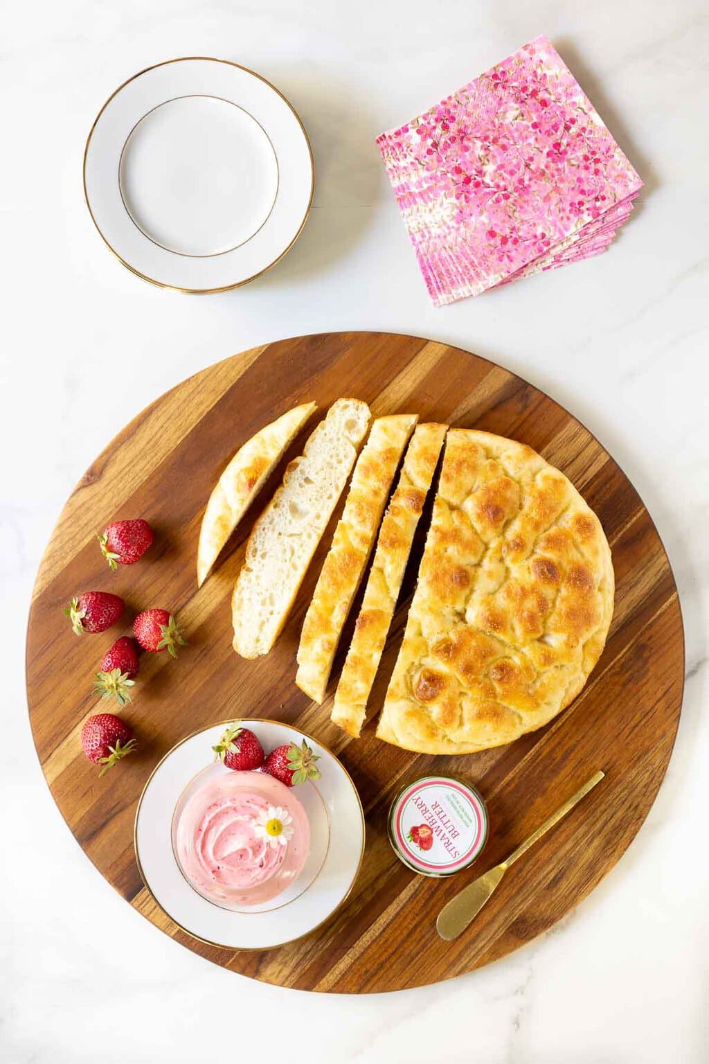 Vertical overhead extreme closeup photo of a jar of Ridiculously Easy Fresh Strawberry Butter on a wood serving plate surrounded by fresh strawberries and Focaccia bread.
