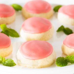 a white serving plate full of Strawberry Lemonade Meltaway cookies decorated with fresh mint leaves and topped with bright pink icing