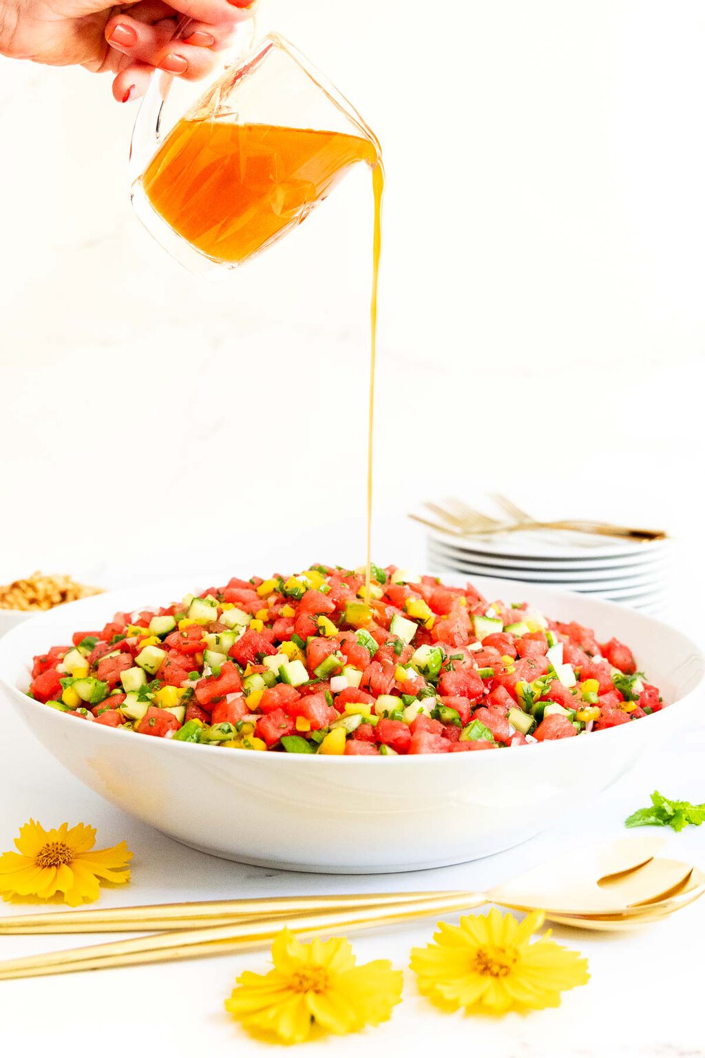 Thai Chopped Watermelon Salad - thecafesucrefarine.com Vertical photo of a person pouring salad dressing over a bowl of Thai Chopped Watermelon Salad.
