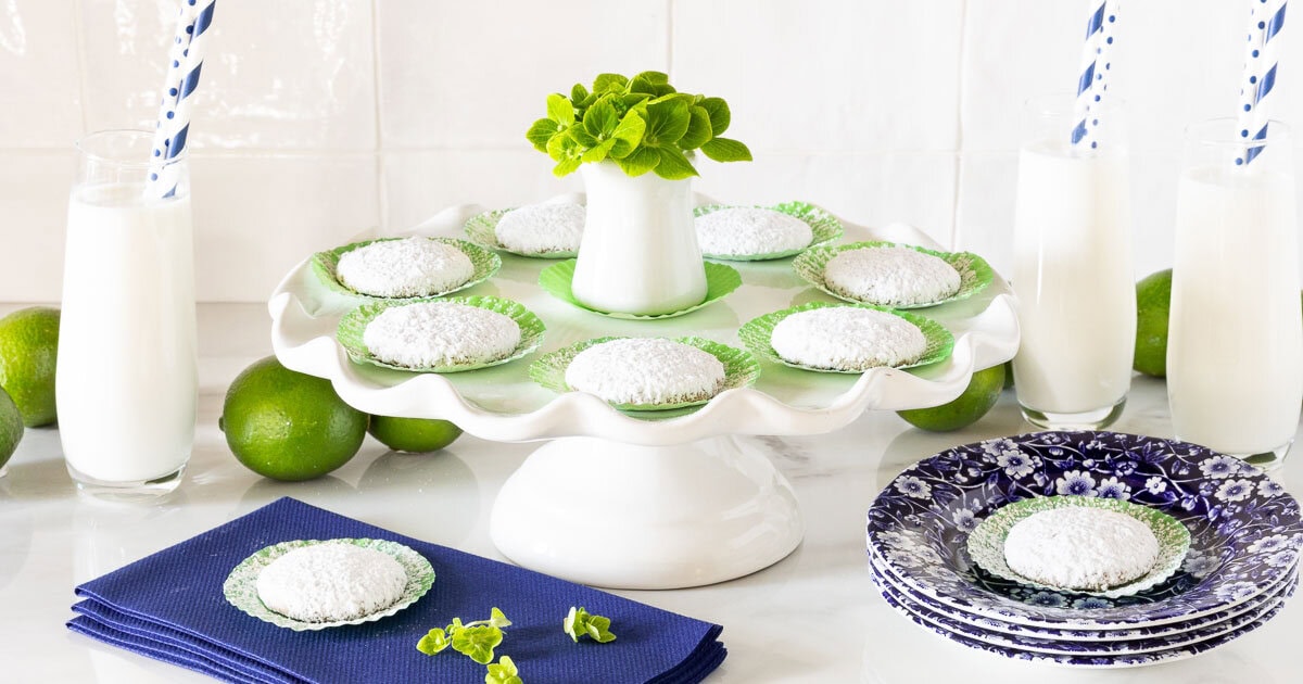 Key Lime Cooler Cookies - thecafesucrefarine.com Horizontal photo of a pedestal serving plate of Key Lime Cooler Cookies surrounded by glasses of milk.