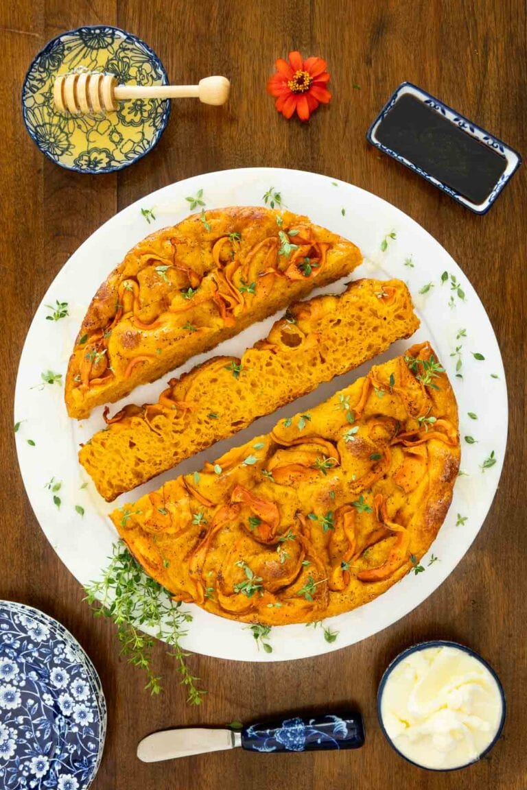 Carrot focaccia with honey and thyme on a round white platter cut into slices