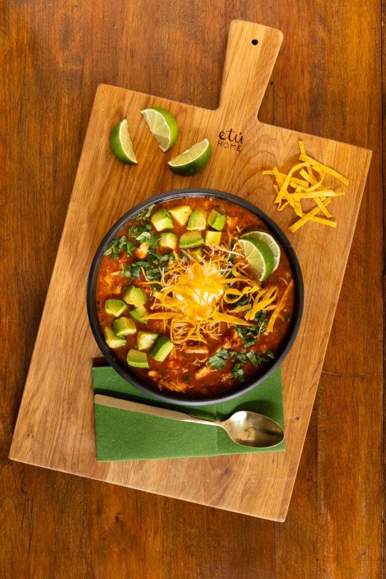 overhead view of chicken poblano tortilla soup topped with avocado cubes, cheddar cheese, limes and greek yogurt