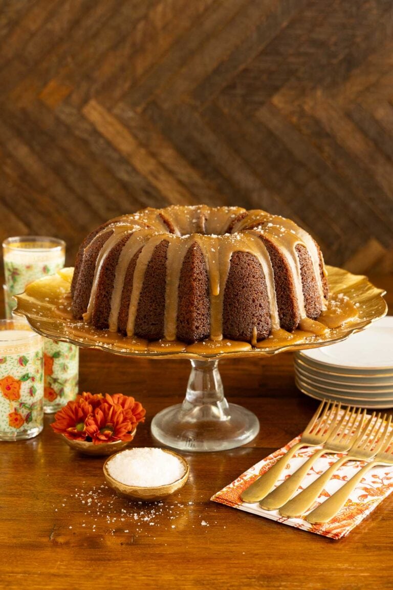 Sweet potato pound cake on a glass cake stand with plates, gold forks and glasses of milk in the background.