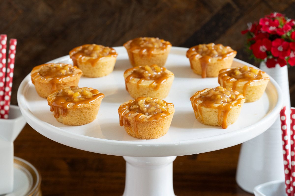 Horizontal photo of a batch of Ridiculously Easy Caramel Apple Shortbread Tarts on a white pedestal serving plate.