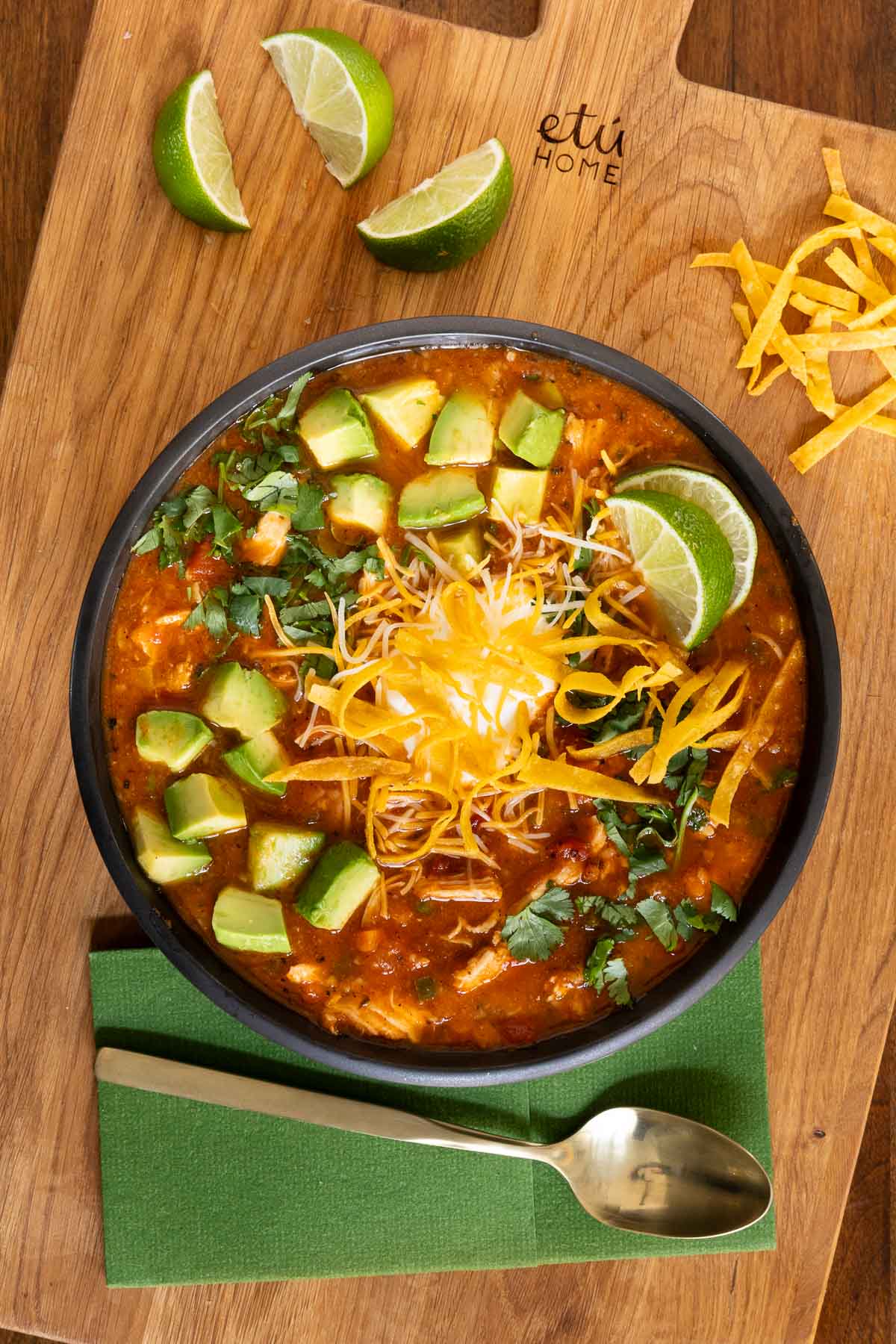 Chicken poblano soup in a bowl with toppings on a wooden cutting board.