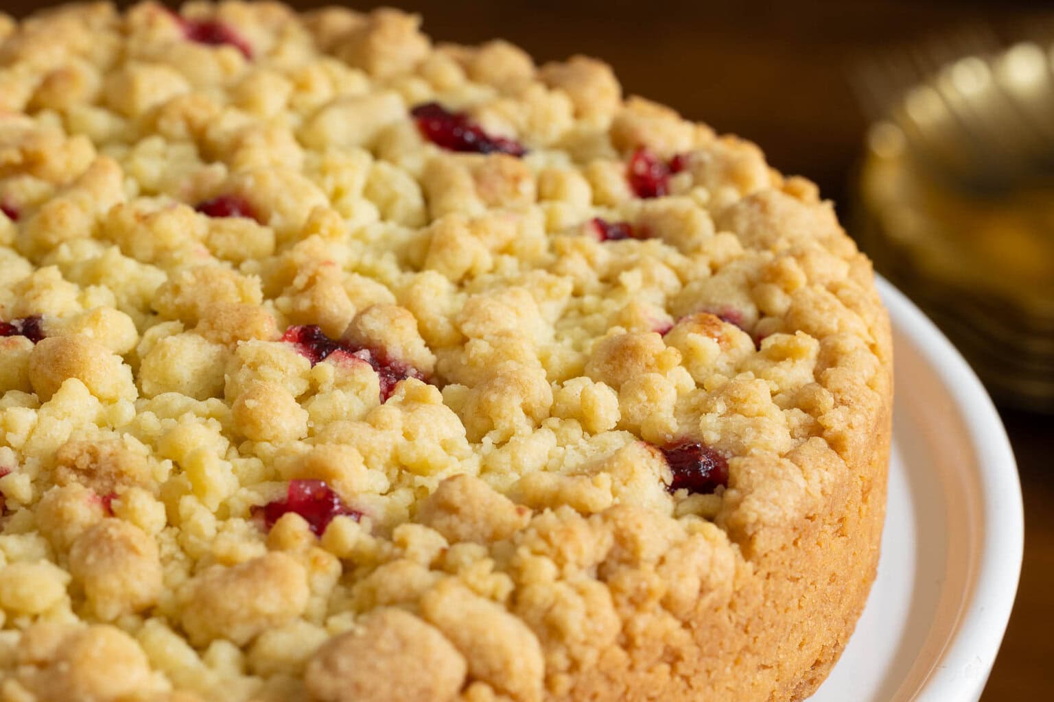 Close up shot of the top and side of a Cranberry Pear Shortbread tart on a white plate with golde serving plates in the background.