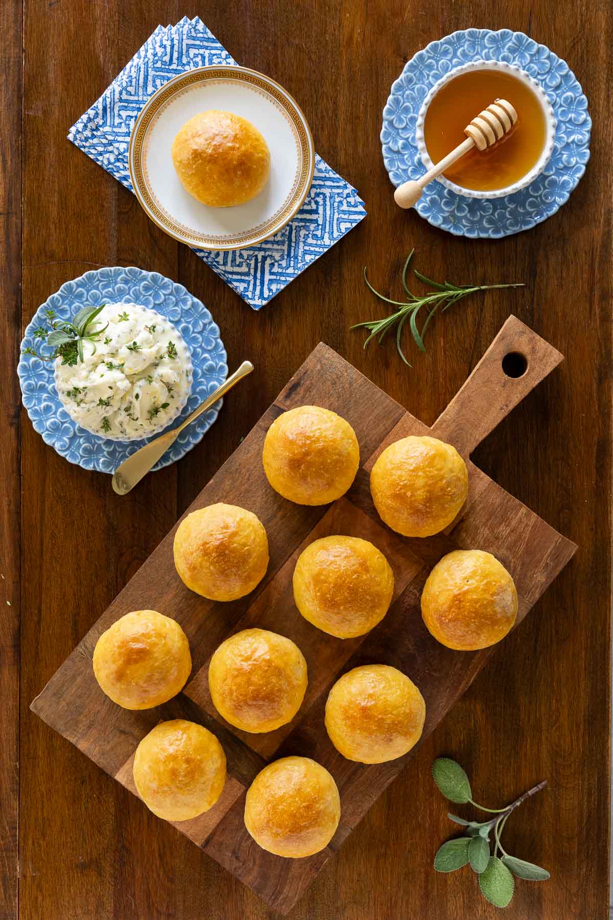 No-Knead Sweet Potato Rolls - thecafesucrefarine.com Vertical overhead photo of a batch of No-Knead Sweet Potato Rolls featuring Herb Butter and honey on a wood cutting board.