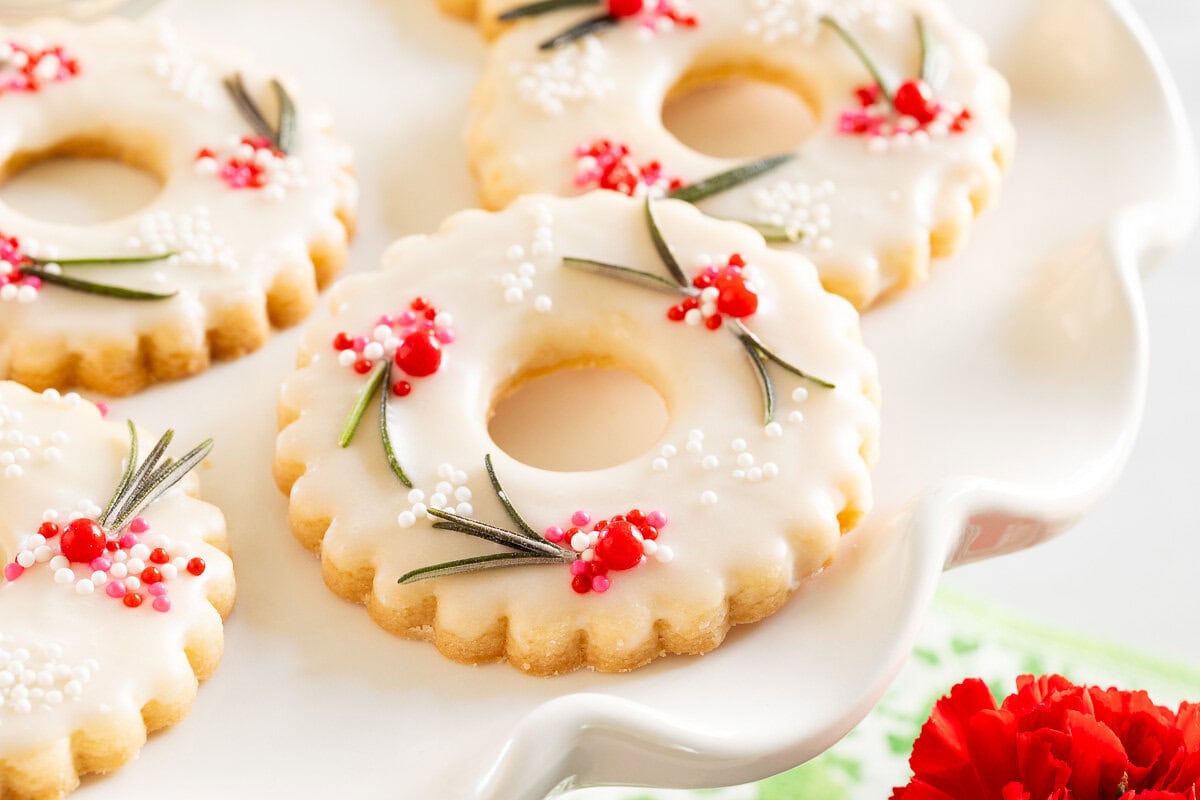 Horizontal extreme closeup photo of a batch of Berries on the Wreath Shortbread Cookies on a white pedestal serving plate.