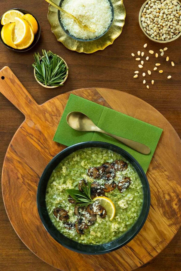 Marry me chicken and spinach risotto in a black bowl on a wooden platter with a green napkin and gold spoon. 