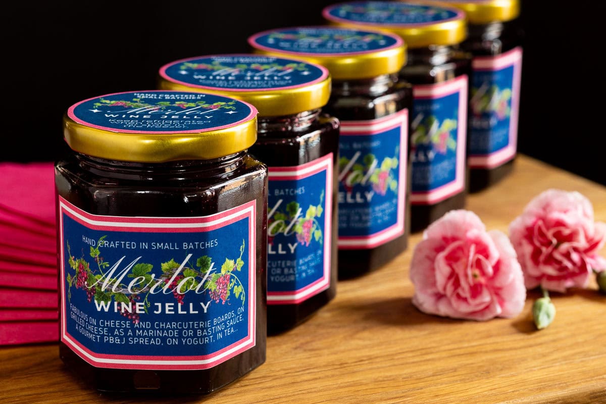 Ridiculously Easy Merlot Wine Jelly - thecafesucrefarine.com Horizontal closeup photo of a row of jars of Ridiculously Easy Merlot Wine Jelly with custom labels for gift giving.