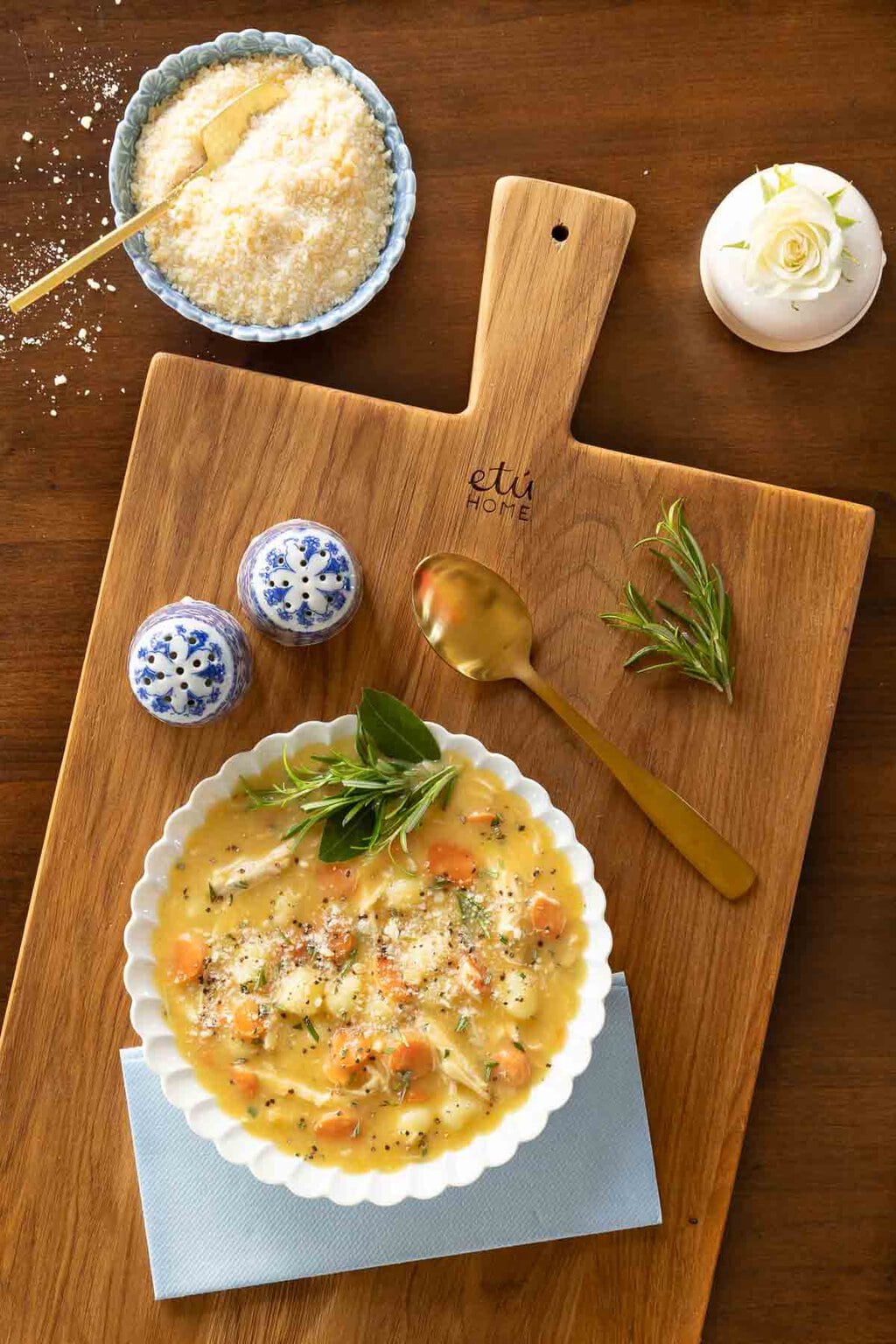 Vertical overhead photo of a bowl of Feel Better Chicken Gnocchi Soup garnished with sprigs of rosemary and grated cheese.