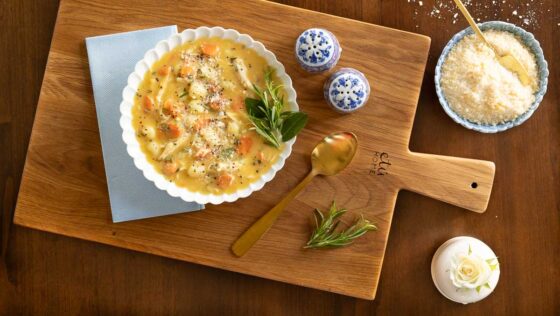 A bowl of Feel-Better Chicken Gnocchi Soup on a wood board garnished with rosemary sprigs.