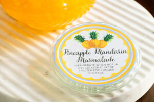 Photo of a yellow, green, and white lid to a Pineapple Mandarin Marmalade jar.