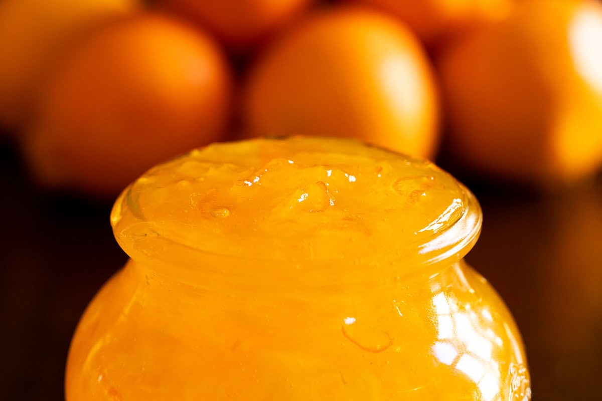 Pineapple Mandarin Marmalade - thecafesucrefarine.com Horizontal extreme closeup photo of a jar of Pineapple Mandarin Marmalade with Mandarin oranges in the background.