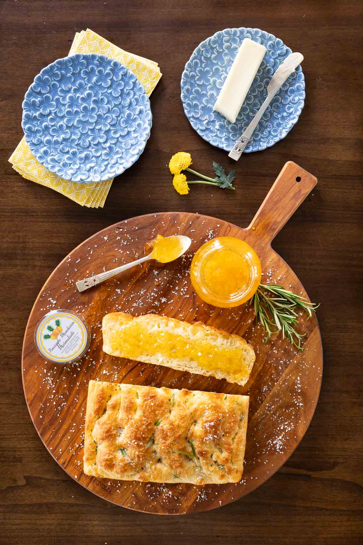 Vertical overhead photo of a loaf of Potato Foccacia (Focaccia Pugliese) on a wood cutting board with a slice covered with Pineapple Mandarin Marmalade.