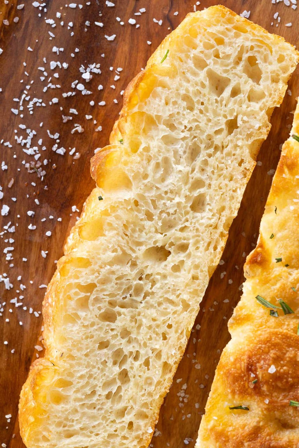 Vertical overhead extreme closeup of a slice of Potato Focaccia (Focaccia Pugliese) on a wood cutting board sprinkled with sea salt.