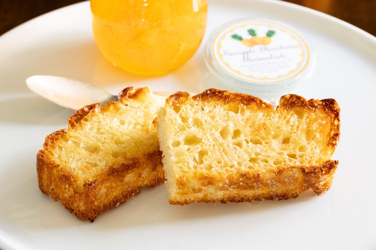 Horizontal closeup photo of two slices of Potato Foccacia (Focaccia Pugliese) toasted with butter and a jar of Pineapple Mandarin Marmalade.