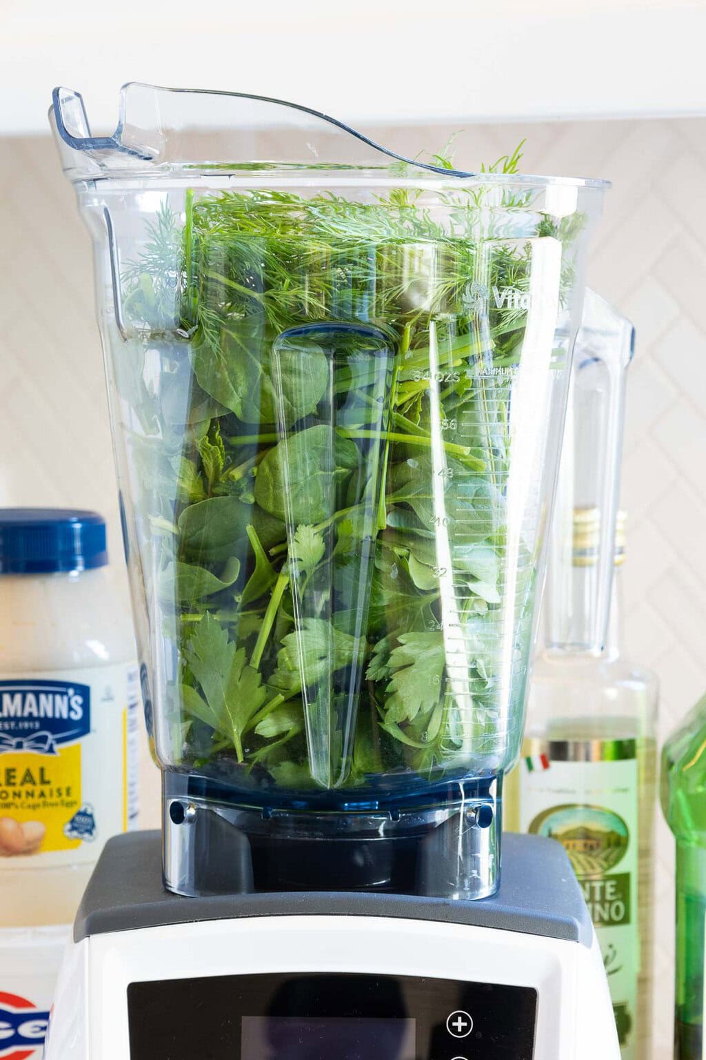 Green Goddess Dressing - thecafesucrefarine.com Vertical closeup photo of a Vitamix filled with fresh herb leaves before blending for making Green Goddess Dressing.