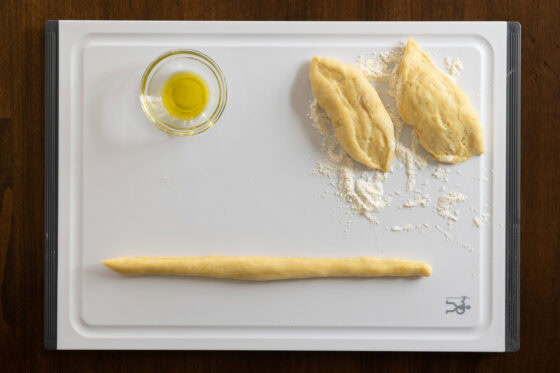 process shot of a long rolled out piece of challah dough on a white cutting board