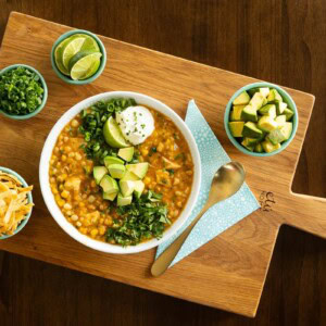 White bean chicken chili on a wooden cutting board with small bowls of toppings.
