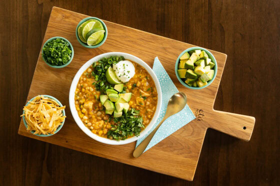 White bean chicken chili on a wooden cutting board with small bowls of toppings.