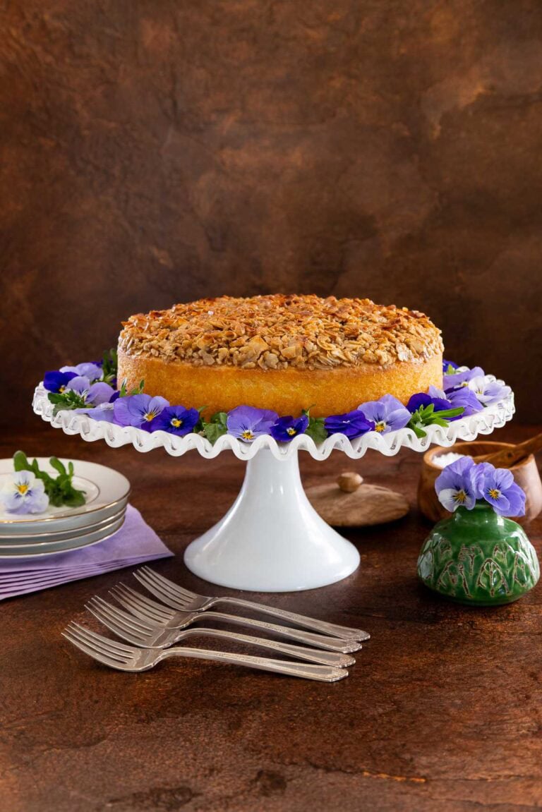Lazy Daisy Cake on a white cake stand with purple flowers.