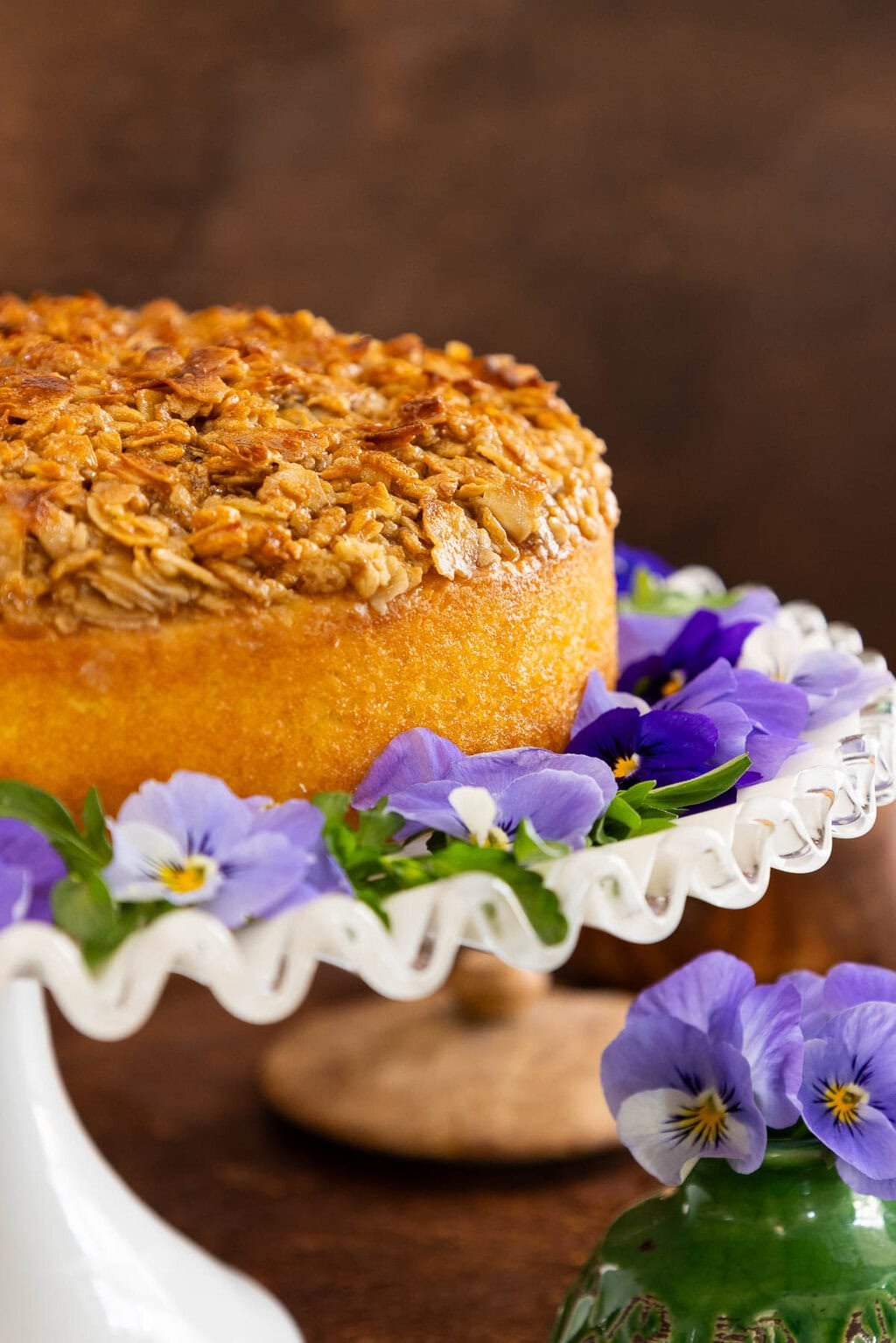 Lazy Daisy Cake on a white cake stand garnished with purple flowers.