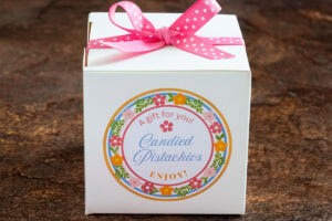 a box of candied pistachios wrapped with a pink ribbon and labeled with a colorful custom label