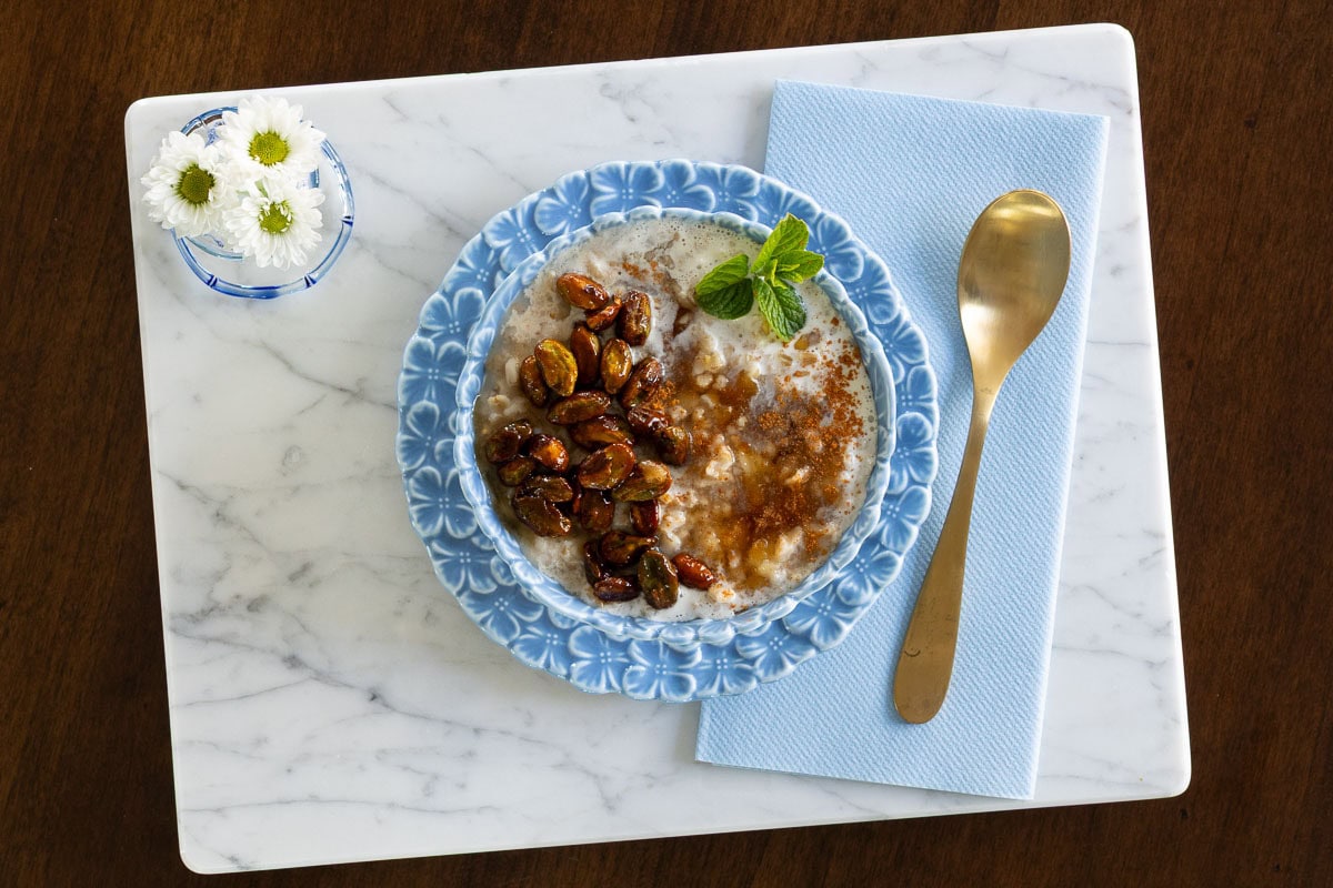 Horizontal overhead photo of a bowl of oatmeal featuring Ridiculously Easy Candied Pistachios on a marble surface.