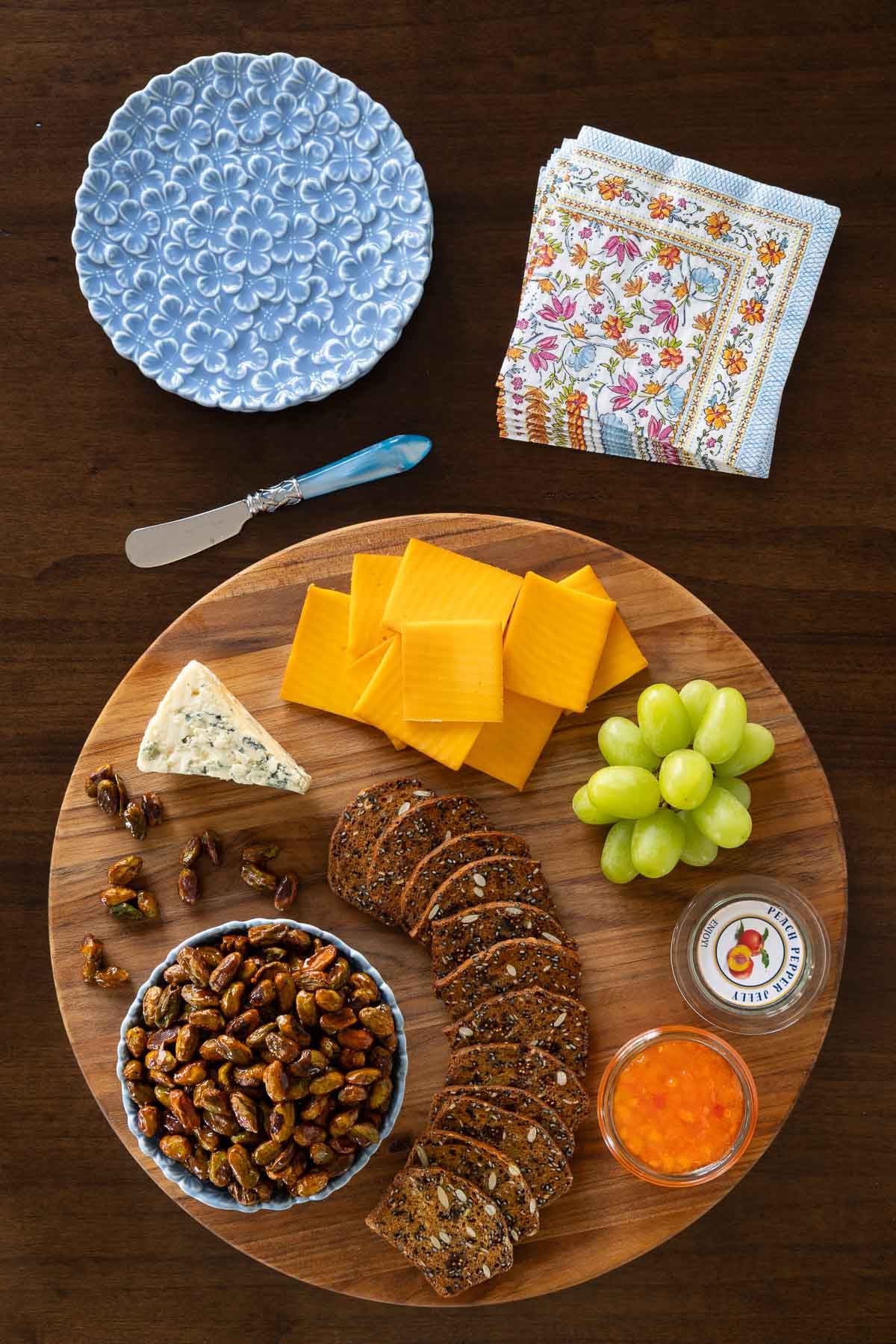 Vertical overhead photo of an appetizer tray filled with cheeses, fresh green grapes, crackers and featuring Ridiculously Easy Candied Pistachios.