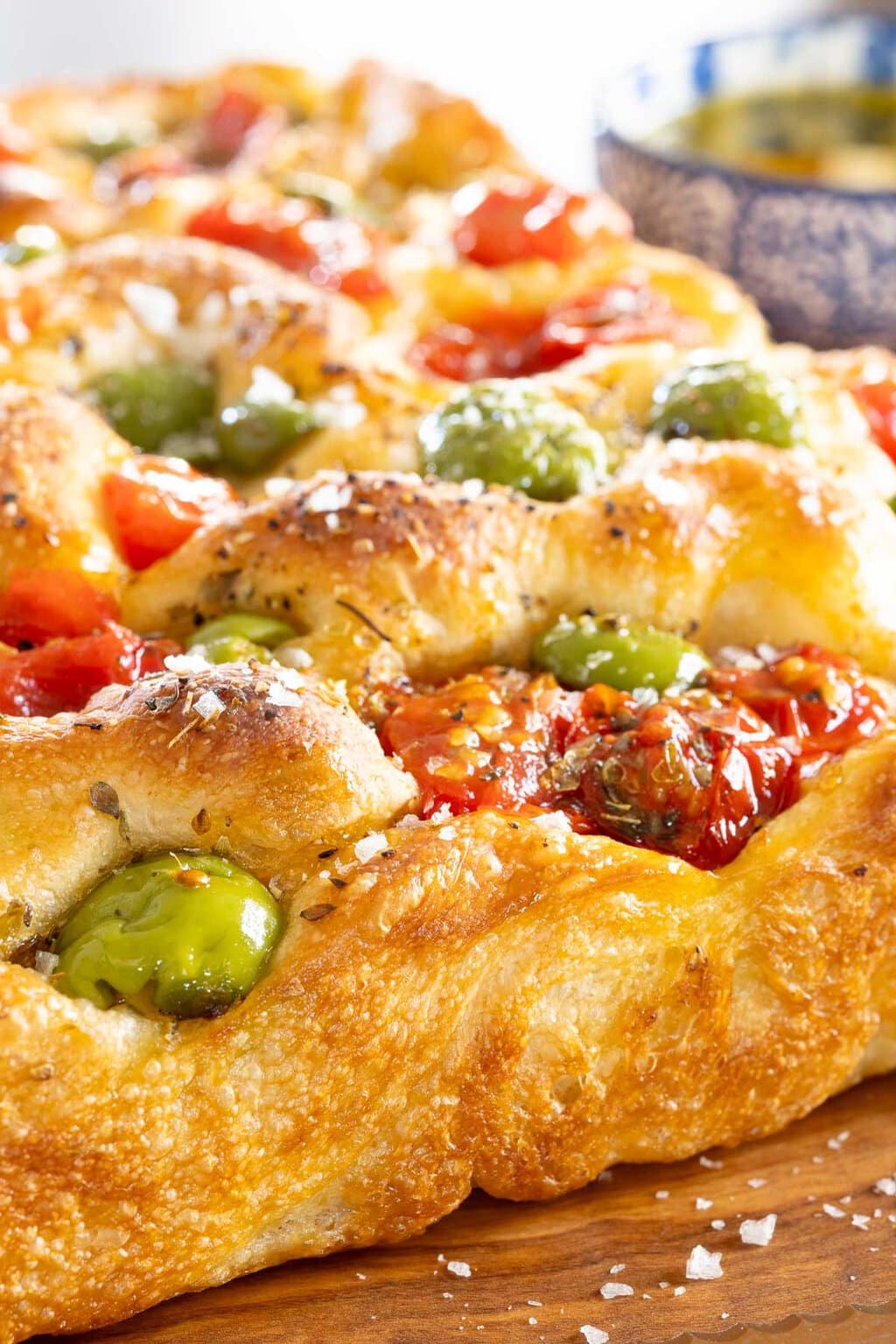 Ridiculously Easy Tomato Olive Focaccia - thecafesucrefarine.com Vertical extreme closeup photo of a loaf of Ridiculously Easy Tomato Olive Focaccia on a wood cutting board.