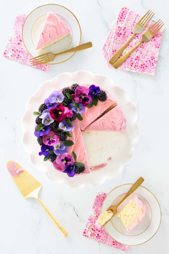 Vanilla Bean Cake with Blackberry Buttercream cake cut into slices and garnished with flowers.