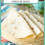 Stack of homemade flour tortillas on a colorful dishtowel.
