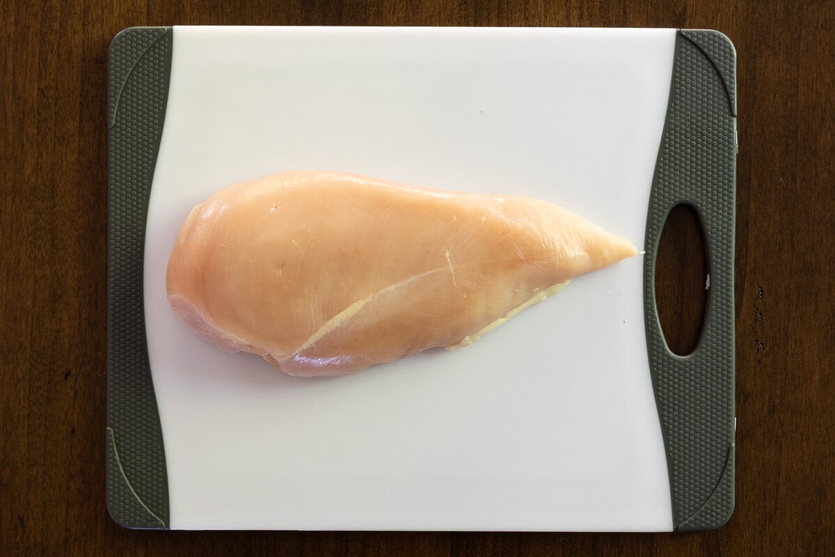 Overhead photo of an uncooked piece of chicken breast on a plastic cutting board.